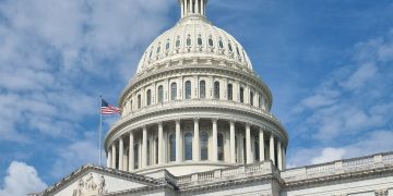 A striking view of the US Capitol dome with flag and blue sky in Washington, DC.