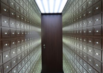 Wooden lockboxes line the walls of a modern, secure vault with a central wooden door.