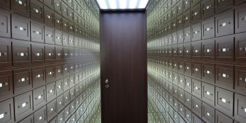 Wooden lockboxes line the walls of a modern, secure vault with a central wooden door.