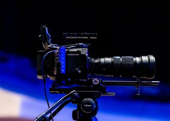 Side view of a professional video camera with lens on a tripod, ready for filming.