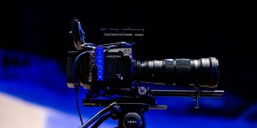 Side view of a professional video camera with lens on a tripod, ready for filming.