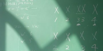 Algebra equations with symbols on a chalkboard in a brightly lit classroom.