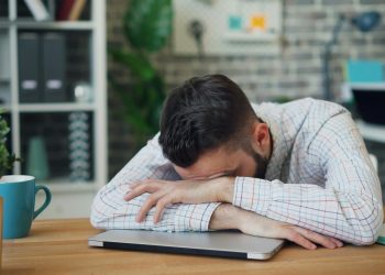 Tired office worker resting head on laptop at desk in a modern office.