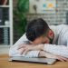 Tired office worker resting head on laptop at desk in a modern office.