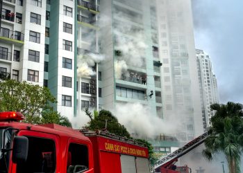 Firefighters respond to a building fire with smoke and emergency vehicles in an urban area.