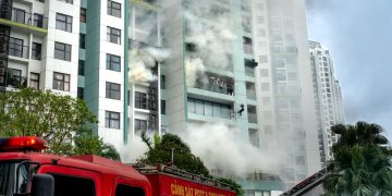 Firefighters respond to a building fire with smoke and emergency vehicles in an urban area.