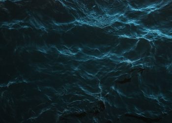Mysterious dark ocean surface with subtle light reflections and deep blue hues.