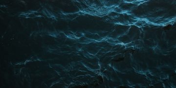 Mysterious dark ocean surface with subtle light reflections and deep blue hues.