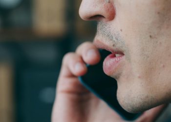 Side profile of an adult speaking on a smartphone indoors.