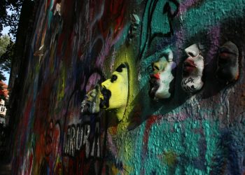 Dynamic street art featuring colorful graffiti and 3D masks on a textured wall.
