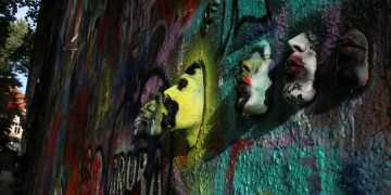 Dynamic street art featuring colorful graffiti and 3D masks on a textured wall.