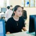 A young Asian woman concentrating on a computer screen in a university classroom.