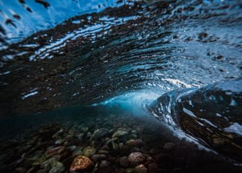 A stunning underwater capture of an ocean wave revealing the pebbles below.