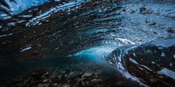 A stunning underwater capture of an ocean wave revealing the pebbles below.