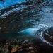 A stunning underwater capture of an ocean wave revealing the pebbles below.