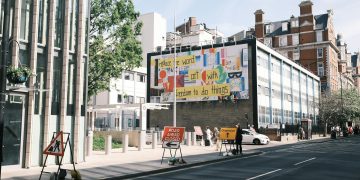 City street scene with a colorful billboard and road closure signs.