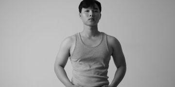 Stylish black and white portrait of an Asian man wearing a tank top in a studio setting.