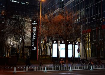 Nighttime city street with illuminated signs and bare trees.