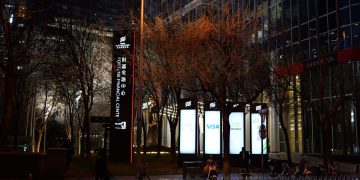 Nighttime city street with illuminated signs and bare trees.