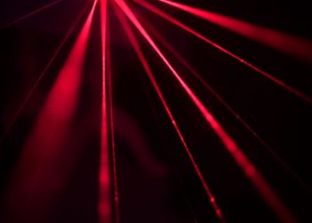 Dynamic red laser beams create a striking abstract pattern in a dark studio setting.