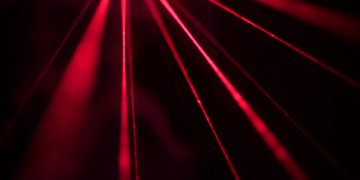 Dynamic red laser beams create a striking abstract pattern in a dark studio setting.