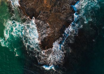 Captivating aerial shot of turquoise waves crashing against a rocky shoreline.
