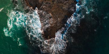 Captivating aerial shot of turquoise waves crashing against a rocky shoreline.