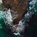 Captivating aerial shot of turquoise waves crashing against a rocky shoreline.