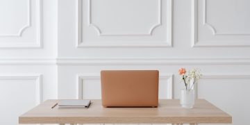 A serene workspace featuring a simple desk with a laptop, notebook, and a vase of flowers.