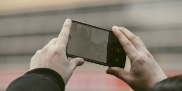 Close-up of hands using a smartphone to capture a photo outdoors.