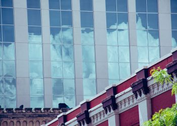 Glass facade reflecting clouds against a decorative urban building.