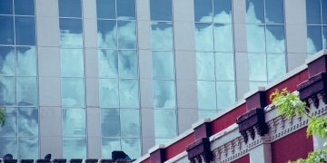 Glass facade reflecting clouds against a decorative urban building.