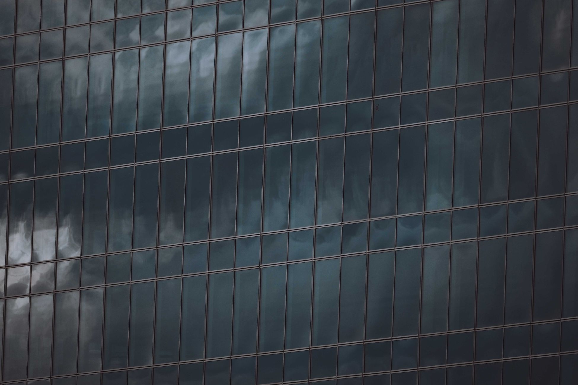 Close-up of a glass building reflecting cloudy skies, creating a dramatic urban scene.