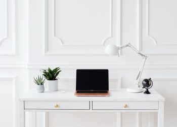 A minimalist home office setup featuring a laptop on a white desk with decor items.