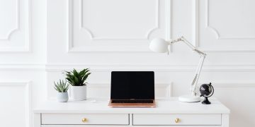 A minimalist home office setup featuring a laptop on a white desk with decor items.