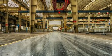 Wide view of an empty industrial warehouse with visible cranes and metal structures.