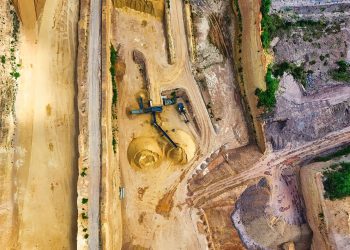An aerial shot of an open-pit mine with machinery and pathways visible, surrounded by landscape.