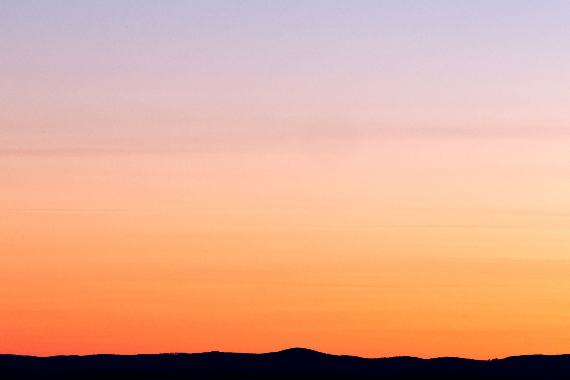 A tranquil sunset with vivid colors over a silhouette of mountains.