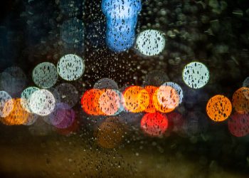 Raindrops on glass with colorful bokeh lights at night, creating a moody urban scene.
