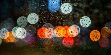 Raindrops on glass with colorful bokeh lights at night, creating a moody urban scene.