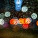 Raindrops on glass with colorful bokeh lights at night, creating a moody urban scene.