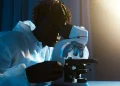 A scientist in protective clothing uses a microscope for research in a laboratory setting.