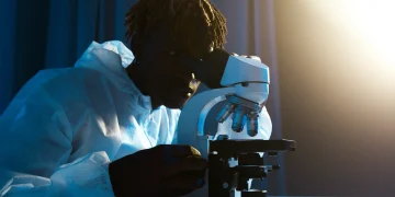 A scientist in protective clothing uses a microscope for research in a laboratory setting.