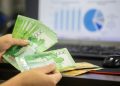 Hands counting cash with financial charts in background, indicating business or finance theme.
