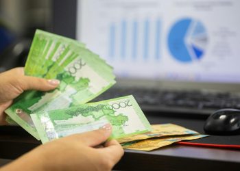 Hands counting cash with financial charts in background, indicating business or finance theme.