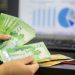 Hands counting cash with financial charts in background, indicating business or finance theme.