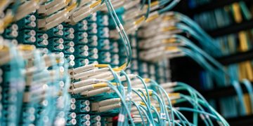 From below of long thin blue cables connected to row of small white connectors on system block in data center