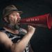 Bearded man shouting through a red megaphone with 'No to A.I' message.