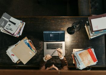 High-angle shot of a busy desk with books, laptop, and lamp, illustrating focused academia.