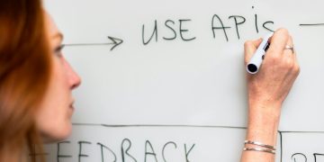 A woman writes 'Use APIs' on a whiteboard, focusing on software planning and strategy.